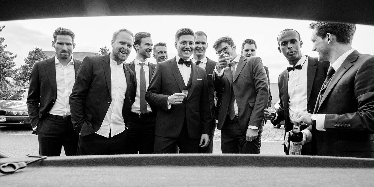 Bräutigam mit seinen Trauzeugen, lachend durch einen geöffneten Kofferraum fotografiert